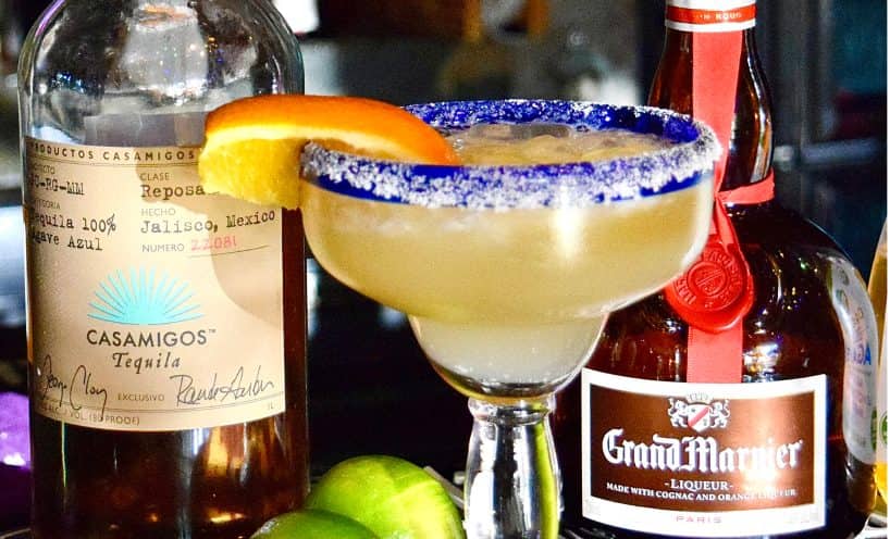 House margarita with orange slice and premium tequila bottles