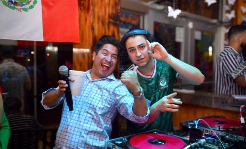 DJ Oteo and guest celebrating by the DJ booth with a Mexican flag